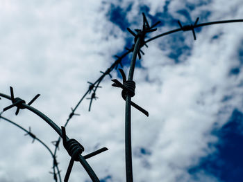 Low angle view of barbed wire against cloudy sky
