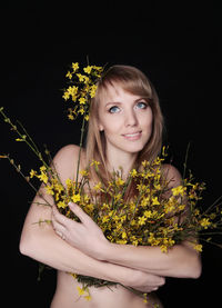 Portrait of beautiful young woman standing by yellow flower against black background