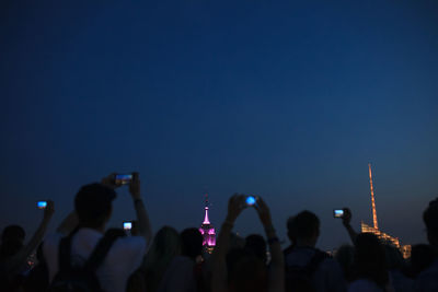 Crowd photographing illuminated empire state building at night against clear blue sky