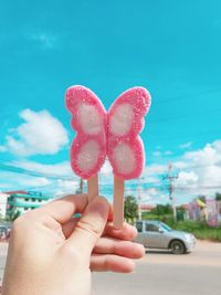 Close-up of hand holding pink butterfly shape candy against sky