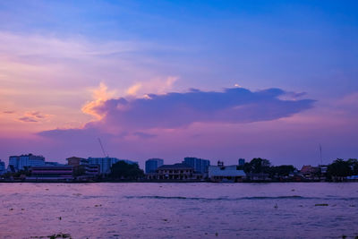 Buildings by sea against sky at sunset