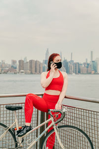 Young woman riding bicycle on railing in city against sky