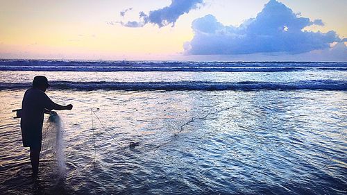 Silhouette man standing by sea against sky during sunset