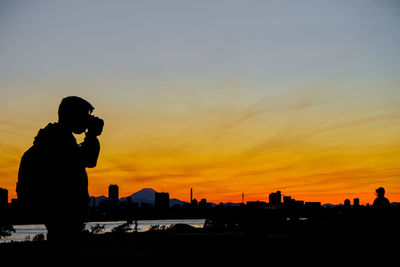 Silhouette of woman photographing at sunset