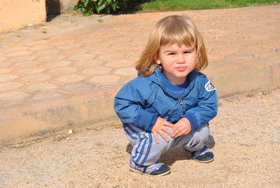 Portrait of cute boy crouching on footpath