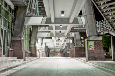 Empty walkway below bridge by building in city