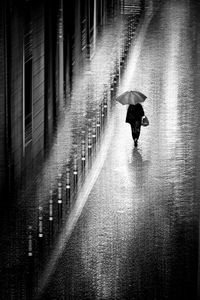 Rear view of man walking on wet road in rainy season