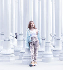 Full length portrait of young woman standing against white wall