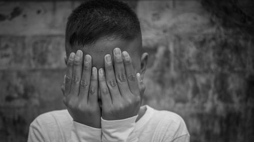 Close-up of teenage boy with face covered by hands