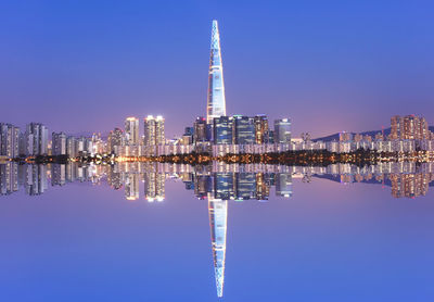 Illuminated modern buildings against clear blue sky at night