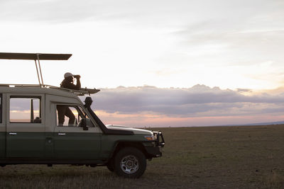 Side view of man looking through binoculars while standing in off-road vehicle