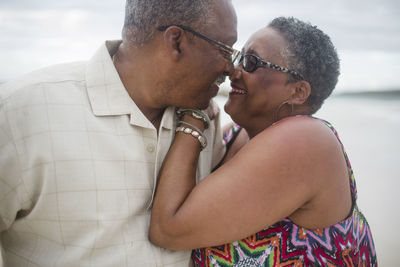 Happy senior couple romancing at beach against cloudy sky