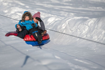 Portrait of mother and son tobogganing on snow covered field