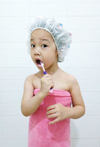 Portrait of cute girl brushing teeth while standing against wall in bathroom