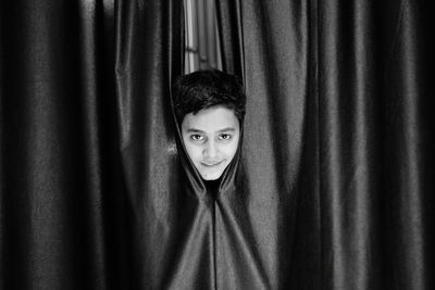 Portrait of young man standing against curtain