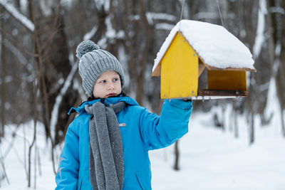 Boy touching bird feeder during winter