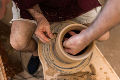Crop unrecognizable sculptor with equipment giving shape while sculpting with brown clay on throwing wheel