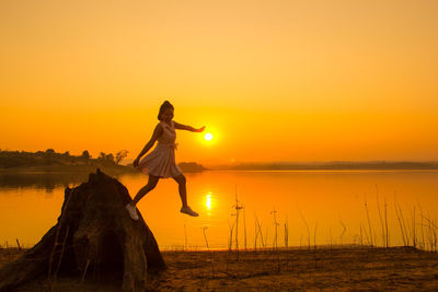 Full length of young woman by lake against sky during sunset
