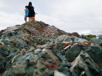 Low angle view of mother with son standing on rock formation against cloudy sky