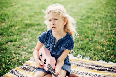 Girl sitting with musical instrument on grass