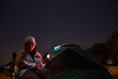 Man sitting by tent against sky at night