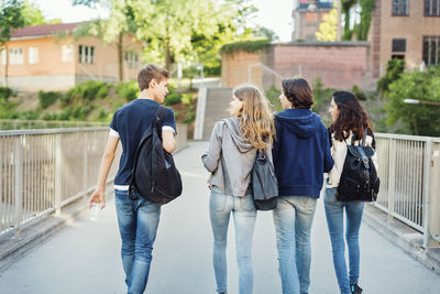 Rear view of teenagers talking while walking on bridge in city