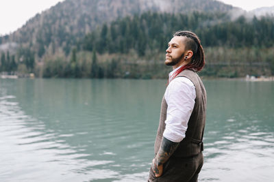 A brutal male hipster groom in a wedding suit in nature by the mountains and lake