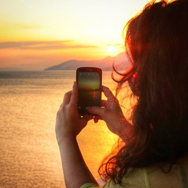 sunset, photography themes, technology, lifestyles, holding, photographing, smart phone, leisure activity, wireless technology, camera - photographic equipment, mobile phone, digital camera, communication, sky, sea, sun, person, young women