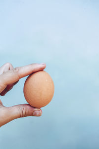 Close-up of hand holding apple against blue sky