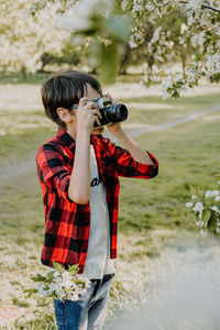 Rear view of boy photographing with arms outstretched standing against plants