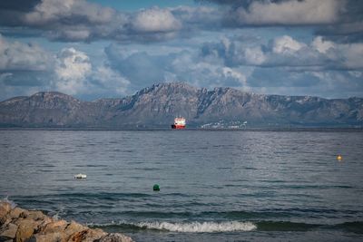 Scenic view of sea by mountain against sky