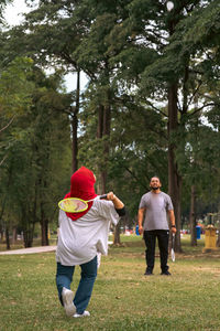 Asian family playing badminton in the park. woman in hijab, view from behind.