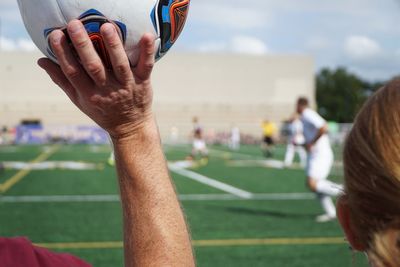 Hand holding ball against sports ground