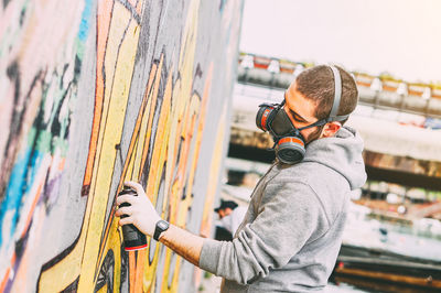 Side view of man photographing graffiti on wall