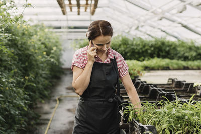 Female gardener talking on mobile phone while working in greenhouse