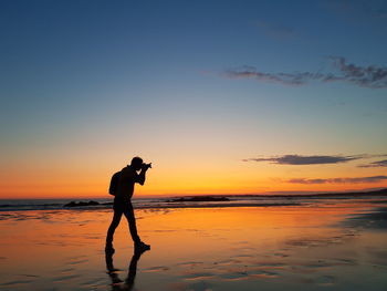 Silhouette man photographing at beach against sky during sunset