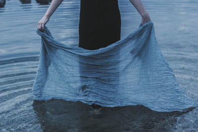 Low section of woman holding textile while standing in sea