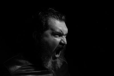Side view of bearded mid adult man screaming against black background