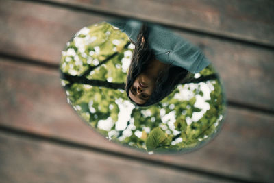 High angle view of girl reflecting in mirror on wood