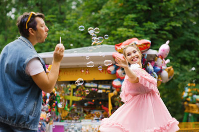 Young happy couple in love having fun in an amusement park with soap bubbles person