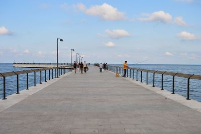 People on pier over sea against sky