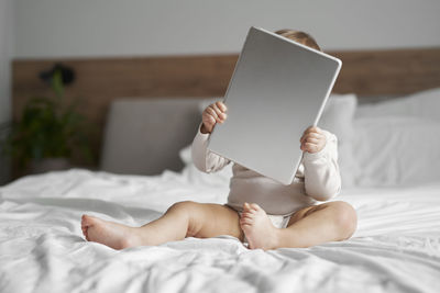 Cute girl holding digital tablet sitting on bed