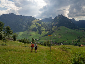 Rear view of people on field by mountains against sky