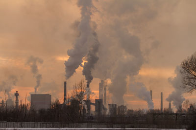 Smoke emitting from factory against cloudy sky during sunset