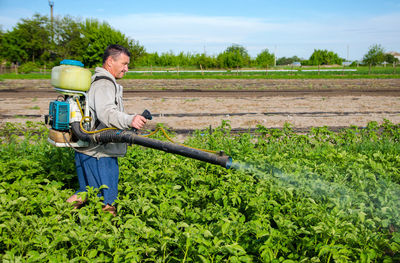 Male farmer with a mist sprayer processes potato bushes with chemicals. control of use of chemicals