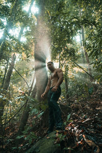 Young man standing by tree in forest