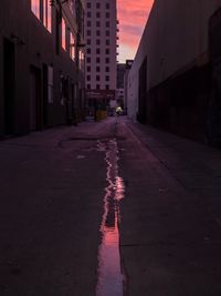 Wet street amidst buildings in city during sunset