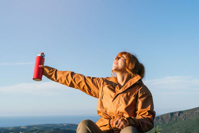 Caucasian hiker standing on top of a mountain holding a bottle of water looking at the sky. 