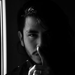 Close-up portrait of young man with finger on lips in darkroom