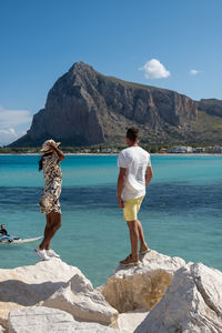 Rear view of woman standing on rock by sea against sky